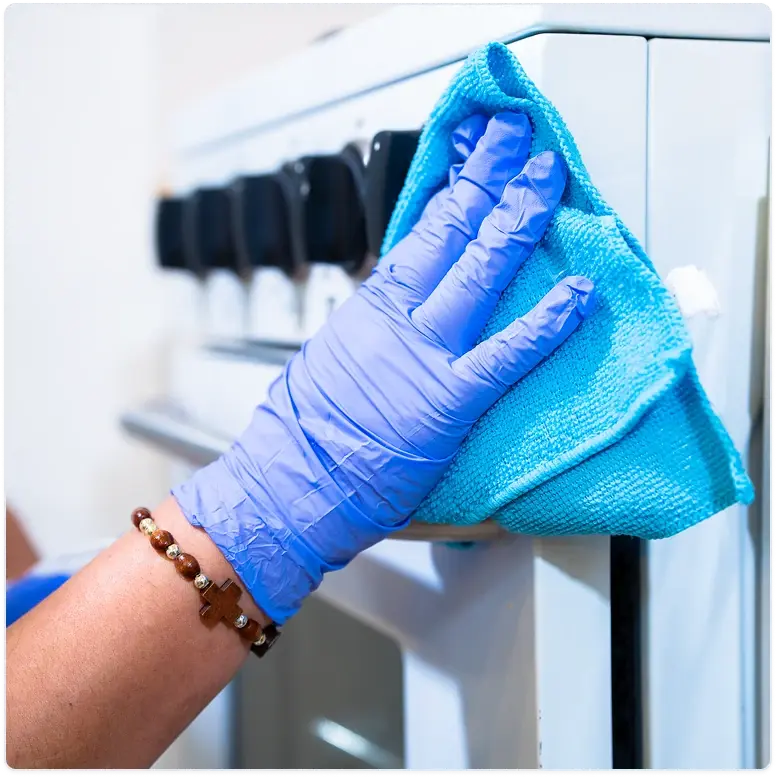 Cleaner wearing blue gloves wiping a kitchen stovetop with a blue cloth