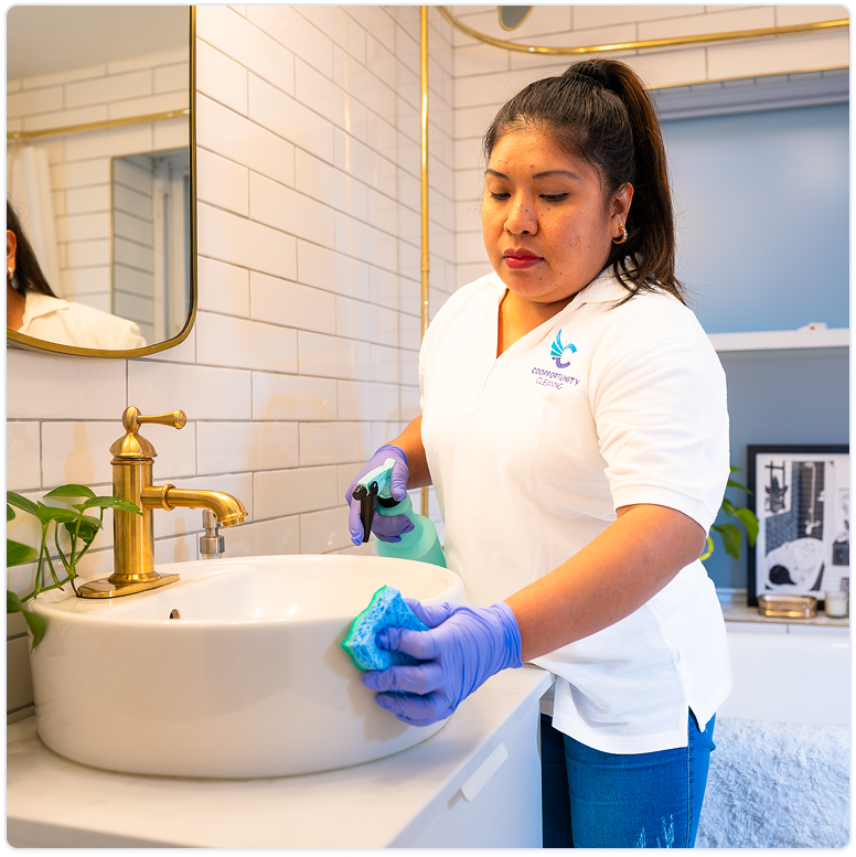 Coopportunity Cleaning professional cleaning a bathroom sink with care, wearing gloves and a cooperative uniform.