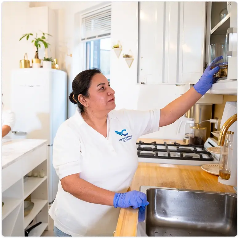 Professional cleaner in white uniform and blue gloves wiping a kitchen sink