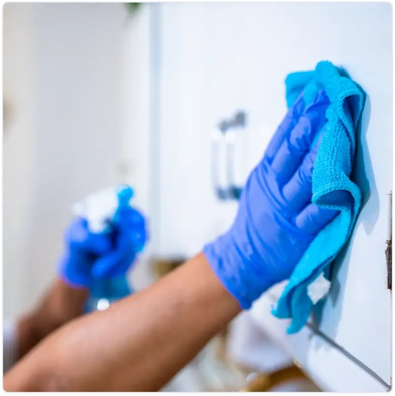 Cleaner wearing blue gloves wiping a glass shower door with a blue cloth